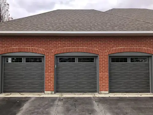 A red brick building with three gray garage doors, each featuring a row of small windows at the top.