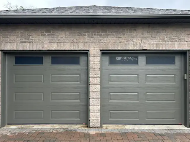 Gray double garage doors set in a light brick wall, each with upper windows.