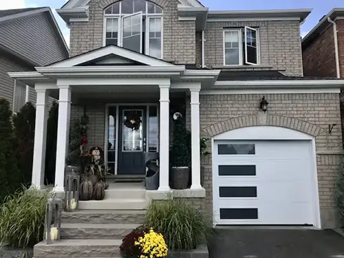 Two-story brick house with a front porch, white columns, and a modern garage door.