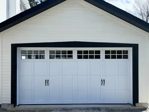 A white garage door with black trim features four panels, each with small square windows at the top.