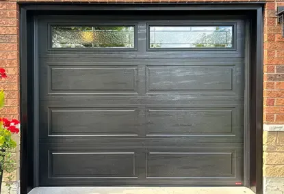 Modern black garage door with rectangular panels, frosted glass windows at the top, and durable aluminum capping on the sides.