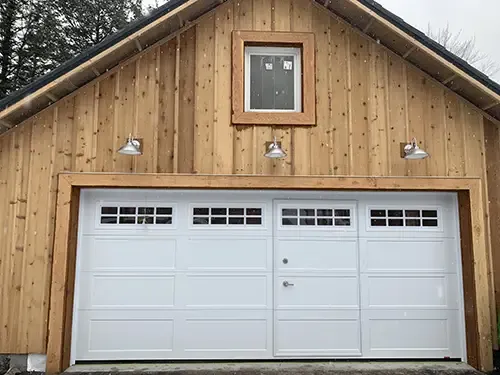 Wood-paneled garage with a large white door featuring small windows and a WalkThru Garage Door integrated into the design.